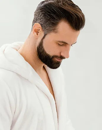 Мъж с брада в халат, демонстриращ стил и поддържан външен вид, използващ Продукти за брада / бръснене.