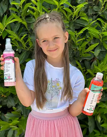 Дете с две бутилки шампоани за деца, усмихнато държи продукти за коса на фона на зеленина.