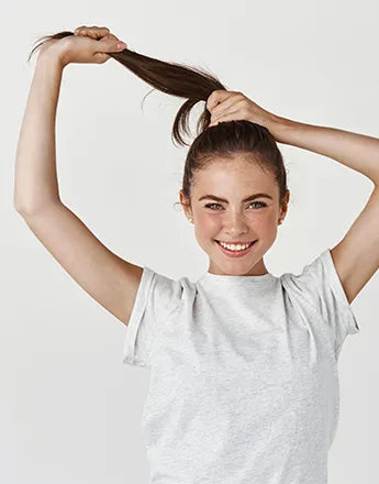 Млада жена с коса, държаща я на опашка, показва усмивка след използване на шампоан за мазен скалп.