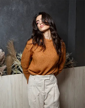 Жена с натурална козметика за коса, носеща уютен оранжев пуловер на фон с растителни елементи.