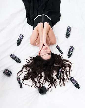 Терапии за коса: жена с дълга коса, разположена на легло с козметични продукти за коса около нея.