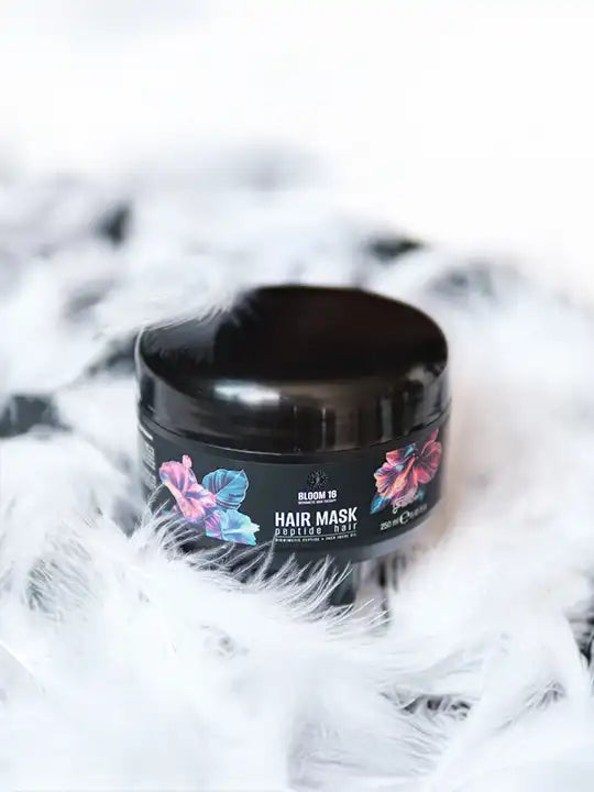 Bloom 16 Възстановяваща грижа за коса – Hair Mask, опакован в черна кутийка сред бели пера.